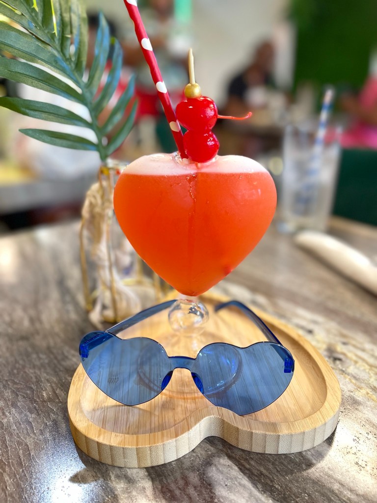 A cocktail in a heart shaped glass paired with heart shaped sunglasses. 